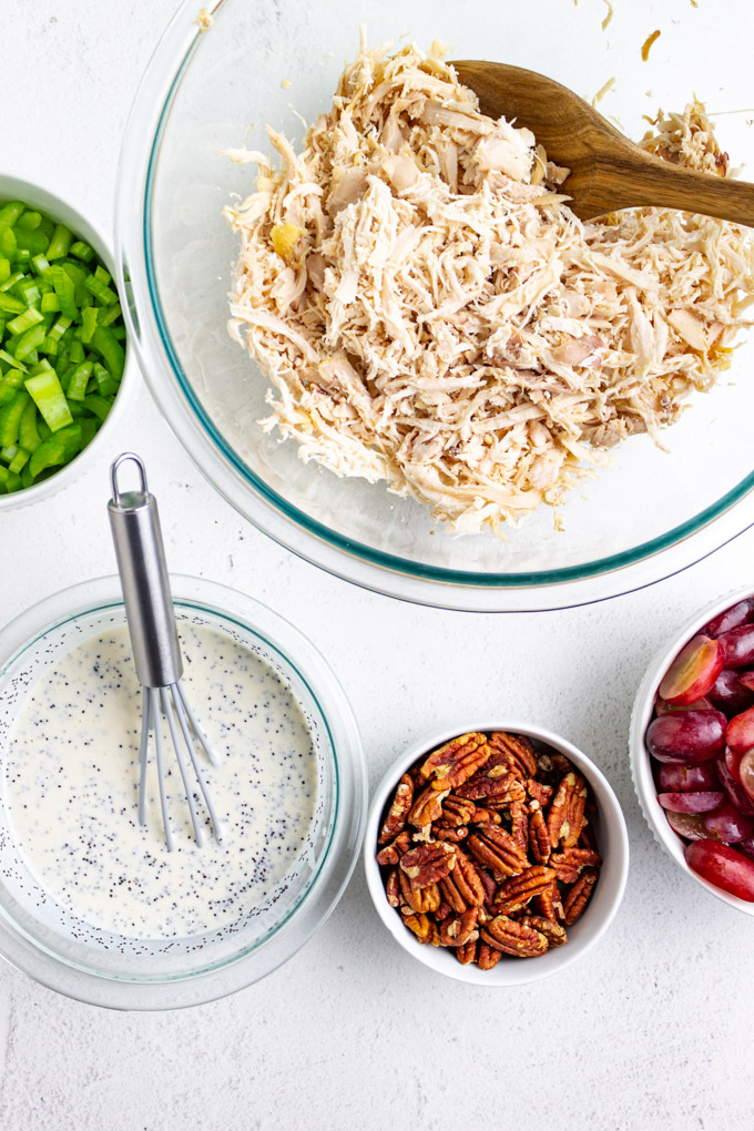 Ingredients in a bowl shredded chicken, chopped celery, dressing, pecans, and grapes.