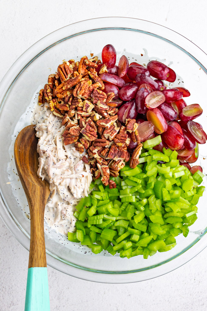 Chicken salad, pecans, grapes, and celery in a bowl with a wooden spoon.