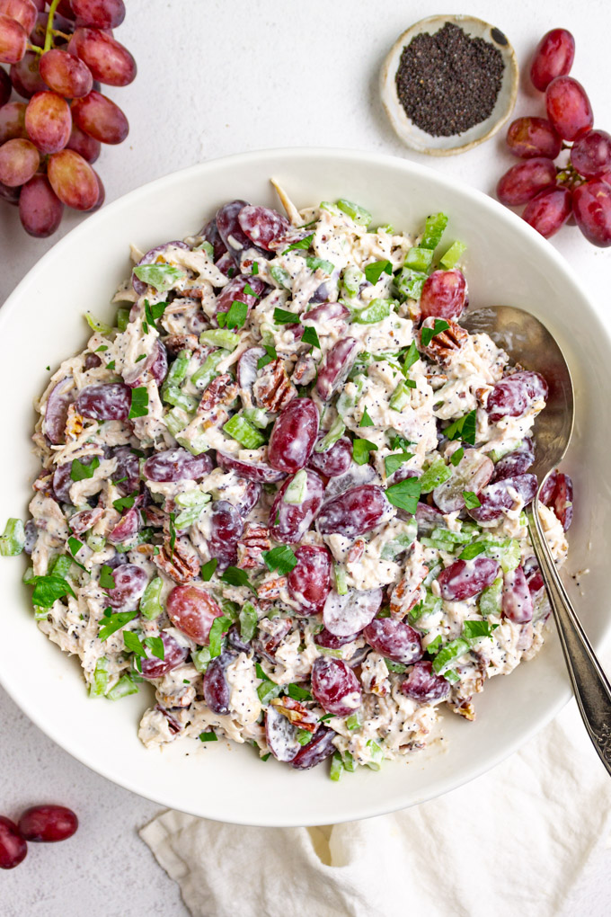 sonoma chicken salad in a white bowl with a serving spoon and grapes off to the side.