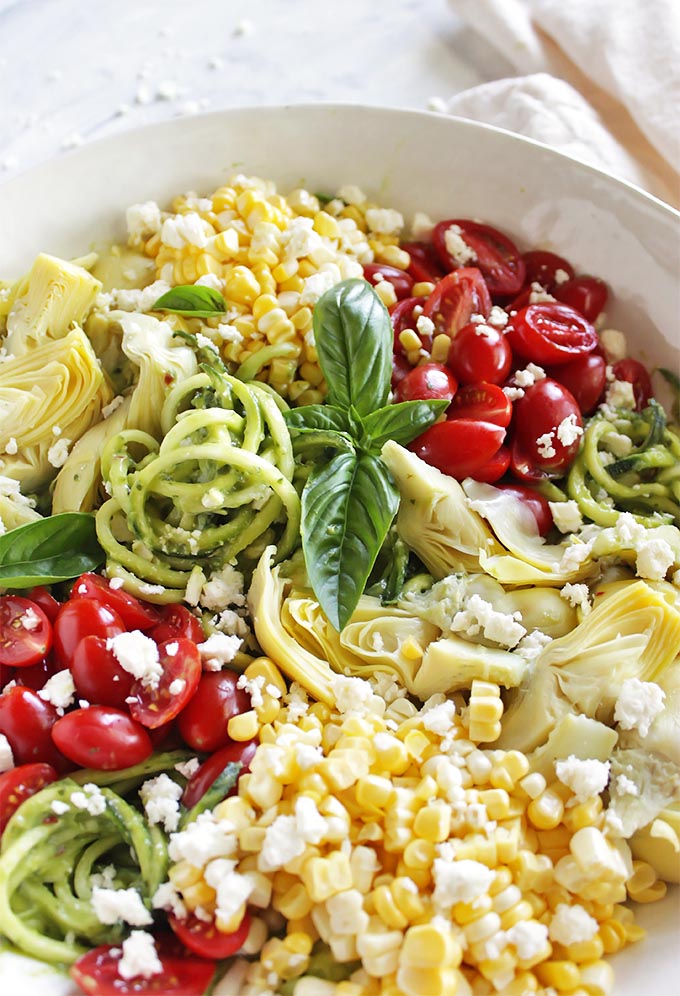 Summer Zucchini Noodle Salad with Creamy Basil Avocado Sauce - This salad is packed with fresh summertime veggies. Zucchini noodles are the base, they are tossed in a basil avocado sauce and that is all topped with fresh corn, grape tomatoes, artichoke hearts, and feta cheese. This recipe only takes 15 minutes to make! It is a great meal or a great side salad to any main dish or is filling enough as an entree . Vegan/vegetarian/gluten free | robustrecipes.com