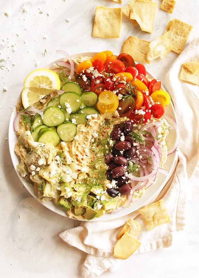 Creamy hummus topped with all the Greek fixings, artichoke hearts, tomatoes, cucumbers, red onion, kalamata olives, feta cheese, avocado, and fresh dill. It's served with sturdy pita chips or gluten free crackers for the ultimate dipping experience. Loaded Greek hummus only takes 20 minutes to make! The perfect appetizer for any party. (Gluten Free & Vegetarian) | robustrecipes.com