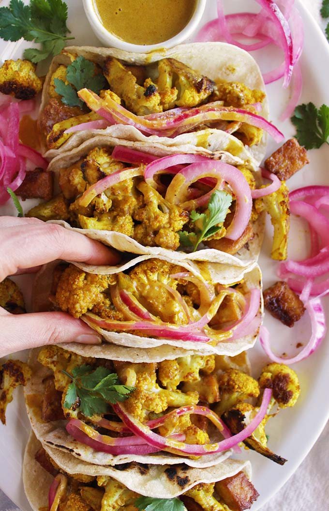 Curried cauliflower tacos with crispy tofu for the ultimate vegan taco night. Topped with crunchy, tangy pickled onions and a creamy curry sauce. Comforting, satisfying, and fun to eat! This recipe is super easy to make, only takes 45 minutes! SO YUM!!! (gluten free/vegan/vegetarian) | robustrecipes.com