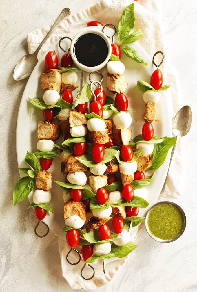Chicken caprese skewers is a fun twist on the classic caprese salad! The skewers are threaded with marinated and grilled chicken, grape tomatoes, fresh mozzarella balls, and fresh basil leaves. They are served with a balsamic glaze and a basil pesto for dipping. Perfect appetizer or entree for summer parties! #chicken #summerrecipes #capresesalad #glutenfree #pesto | robustrecipes.com