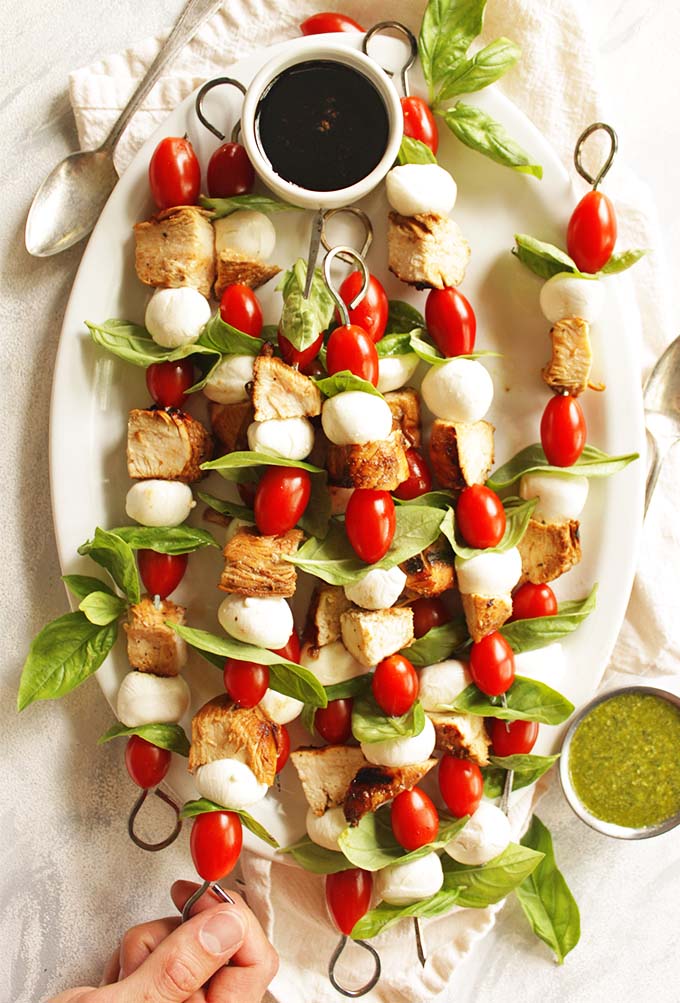 Chicken caprese skewers is a fun twist on the classic caprese salad! The skewers are threaded with marinated and grilled chicken, grape tomatoes, fresh mozzarella balls, and fresh basil leaves. They are served with a balsamic glaze and a basil pesto for dipping. Perfect appetizer or entree for summer parties! #chicken #summerrecipes #capresesalad #glutenfree #pesto | robustrecipes.com