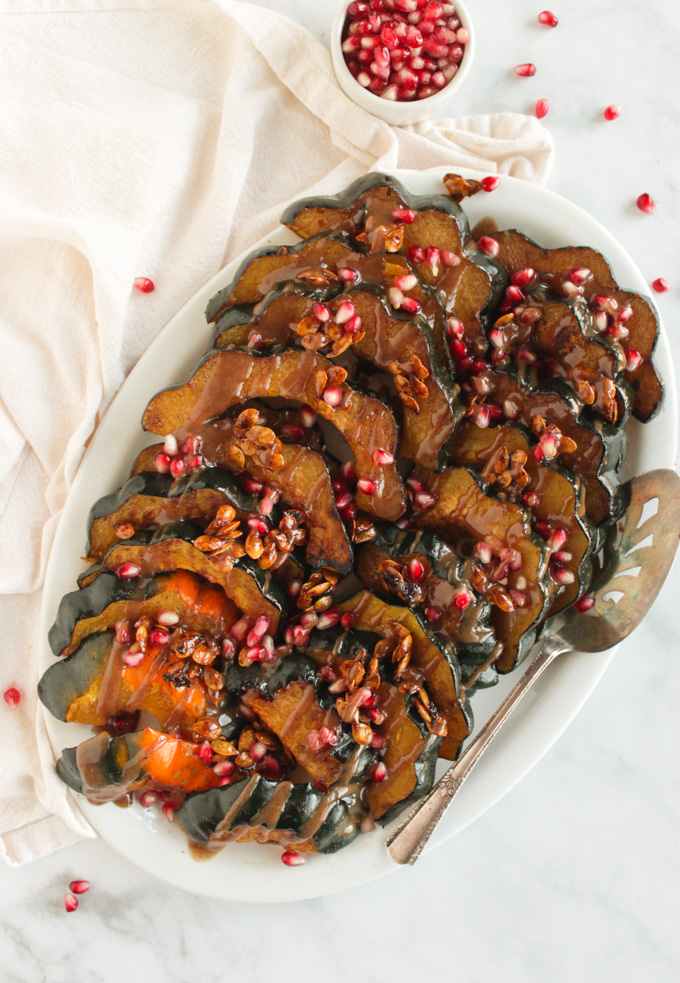 Roasted acorn squash slices topped with maple glazed squash seeds, pomegranate seeds, and cinnamon tahini sauce. Perfect fall or Thanksgiving side dish. #recipe #Thanksgiving #vegan #vegetarian | robustrecipes.com