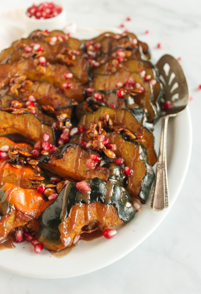 Roasted acorn squash slices topped with maple glazed squash seeds, pomegranate seeds, and cinnamon tahini sauce. Perfect fall or Thanksgiving side dish. #recipe #Thanksgiving #vegan #vegetarian | robustrecipes.com