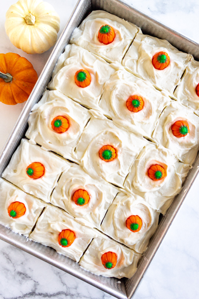 Pumpkin cake in it's 9x13 pan, frosted, and cut into squares with pumpkin candies on each square.