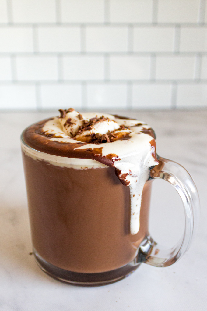 Homemade hot chocolate in a clear mug with melted whipped cream dripping down the side of the mug.
