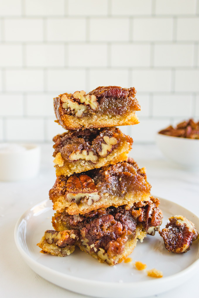 a stack of pecan pie bars with a white tiled background.