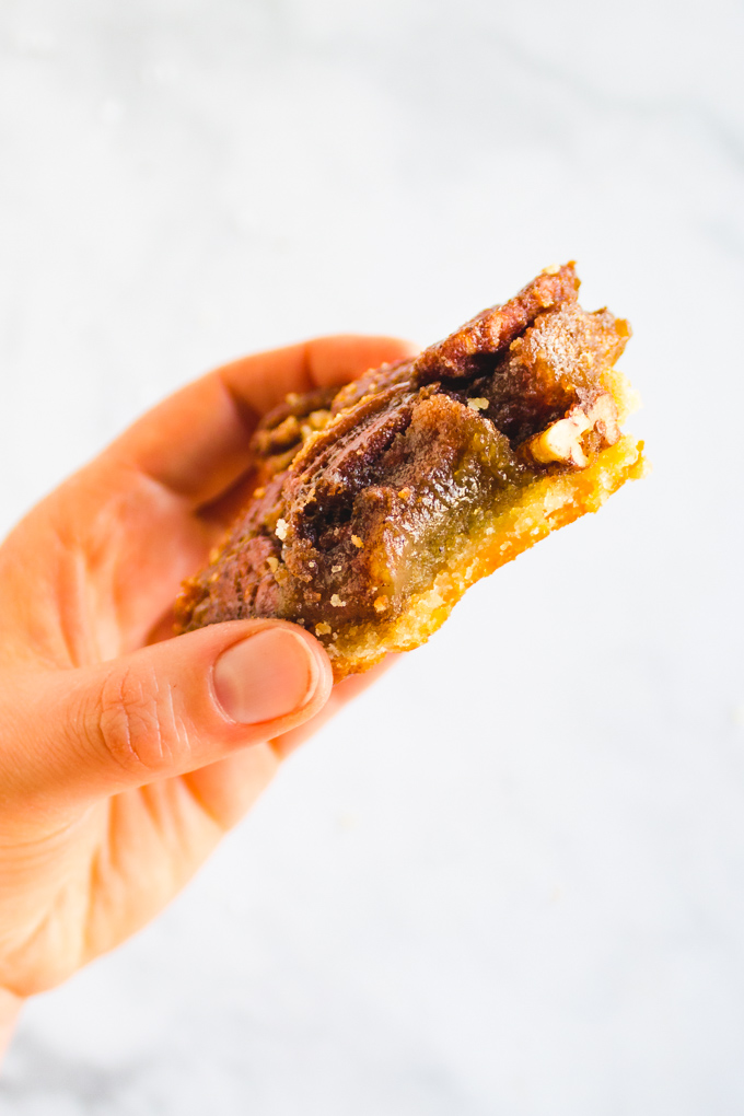 Pecan pie bar with with a bite, held by a hand.