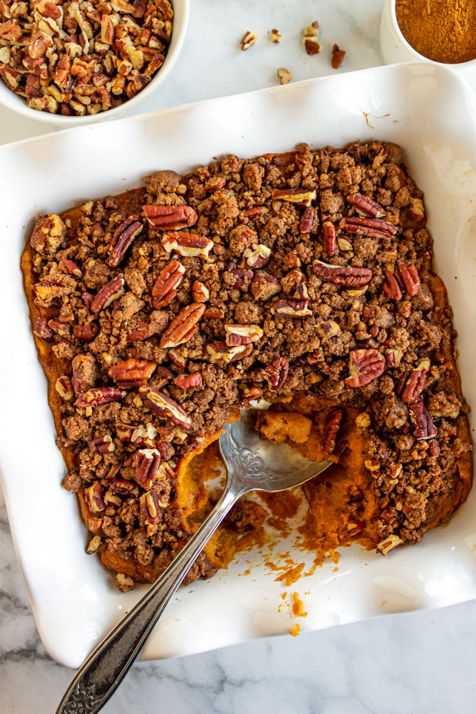 Overhead photo of sweet potato casserole with streusel topping, in a square baking dish, with some casserole scooped out.