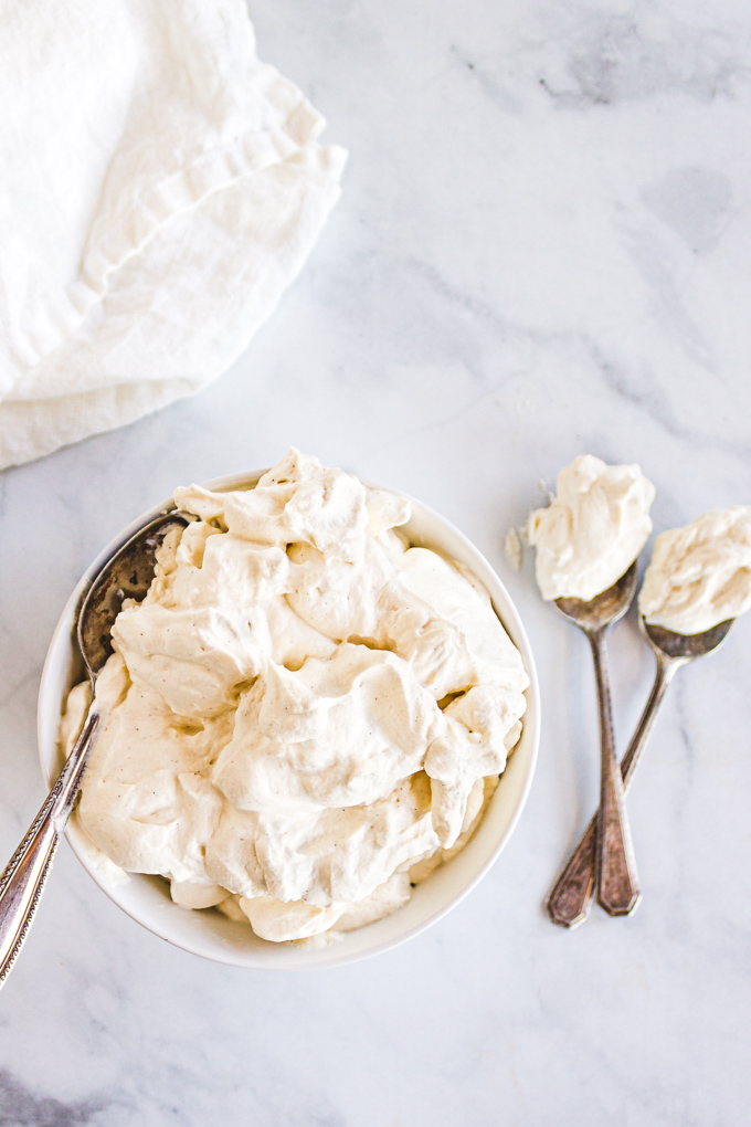 Overhead shot of whipped cream in a white bowl with a spoon and white towel