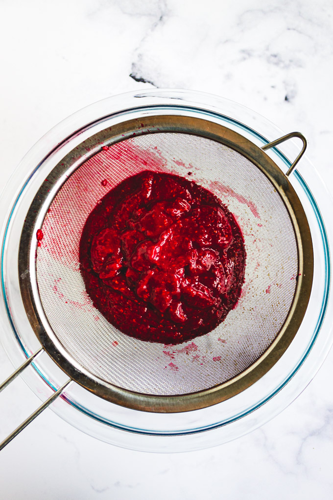 pureed raspberries in a fine mesh sive to be strained into a bowl for raspberry puree.