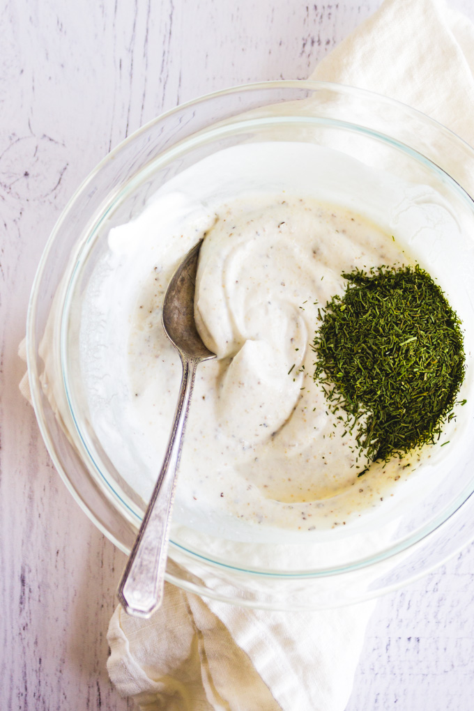 Greek yogurt in a mixing bowl with dill, on a white background.