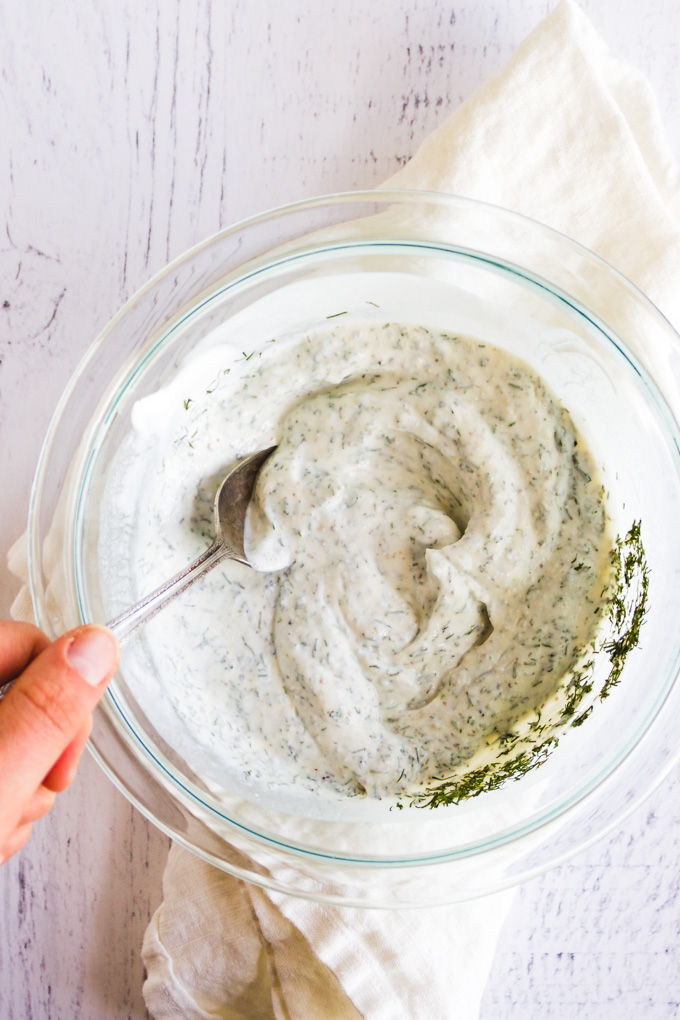 Dill dip mixed up in a mixing bowl on a white background with a spoon in it.