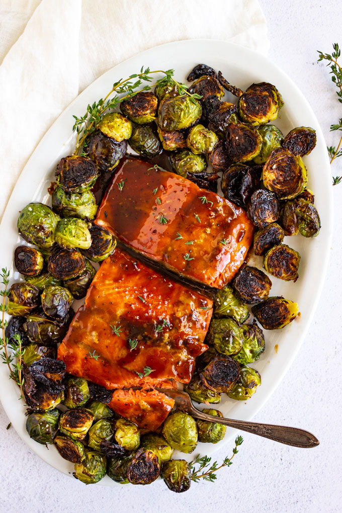 maple glazed salmon on a white oval platter with roasted brussels sprouts.