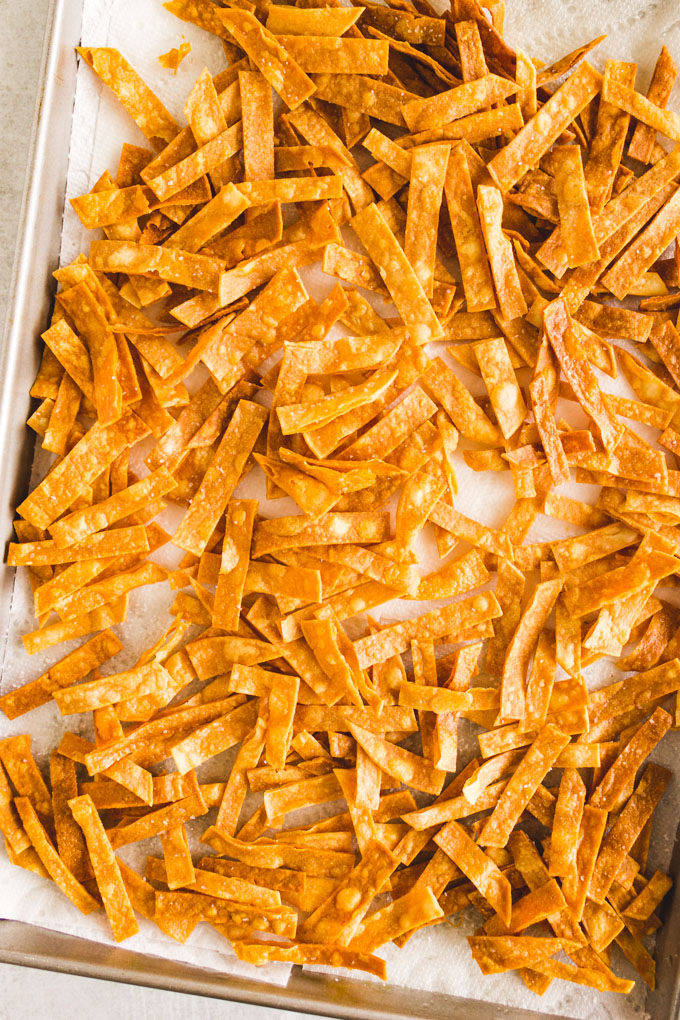 Fried tortilla strips on a baking sheet that's lined with paper towels.