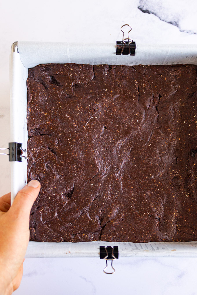 Brownies pressed into a square pan on a marble background, with a hand holding the pan.