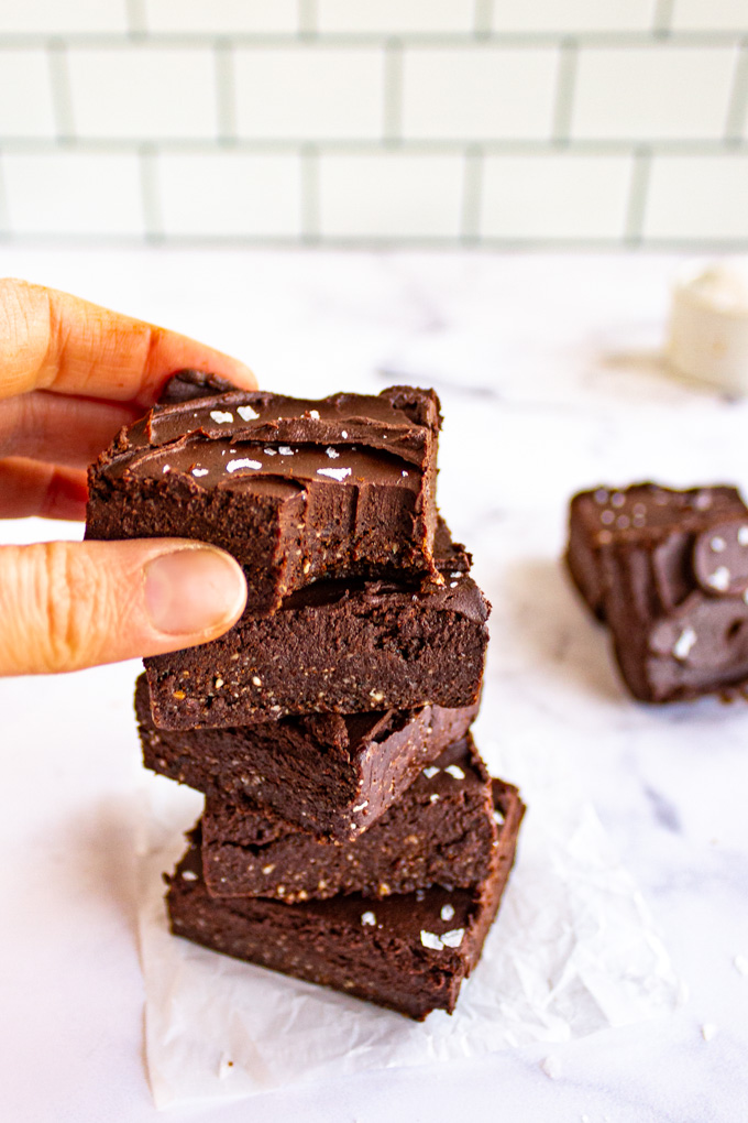 No bake brownies are stacked with a hand reaching for one of them.
