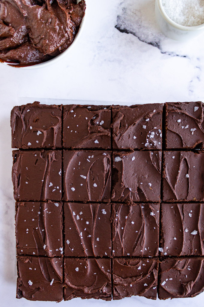 brownies cut into squares with a bowl of vegan chocolate frosting in the corner.
