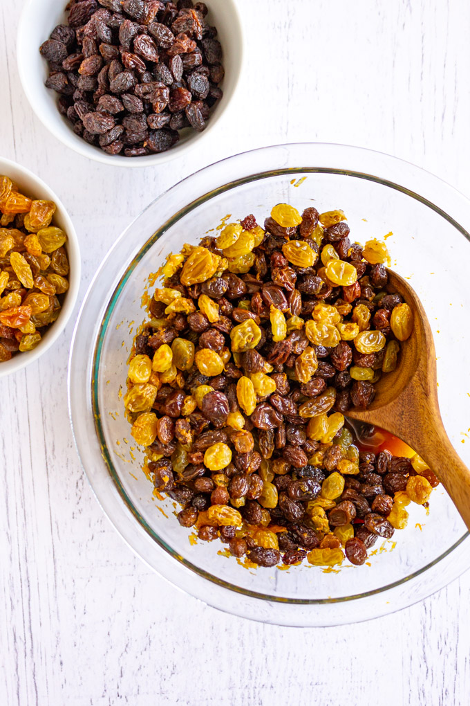 Soaked golden and regular raisins in a mixing bowl with a wooden spoon, on a white background.