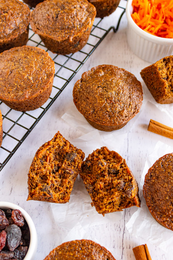 Healthy spiced carrot muffins on a white background with one muffin cut in half and shredded carrots in the background.
