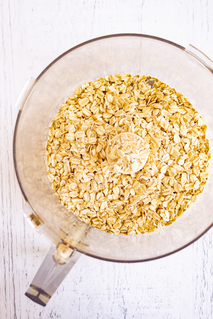 Old fashioned rolled oats in a food processor, on a white background.