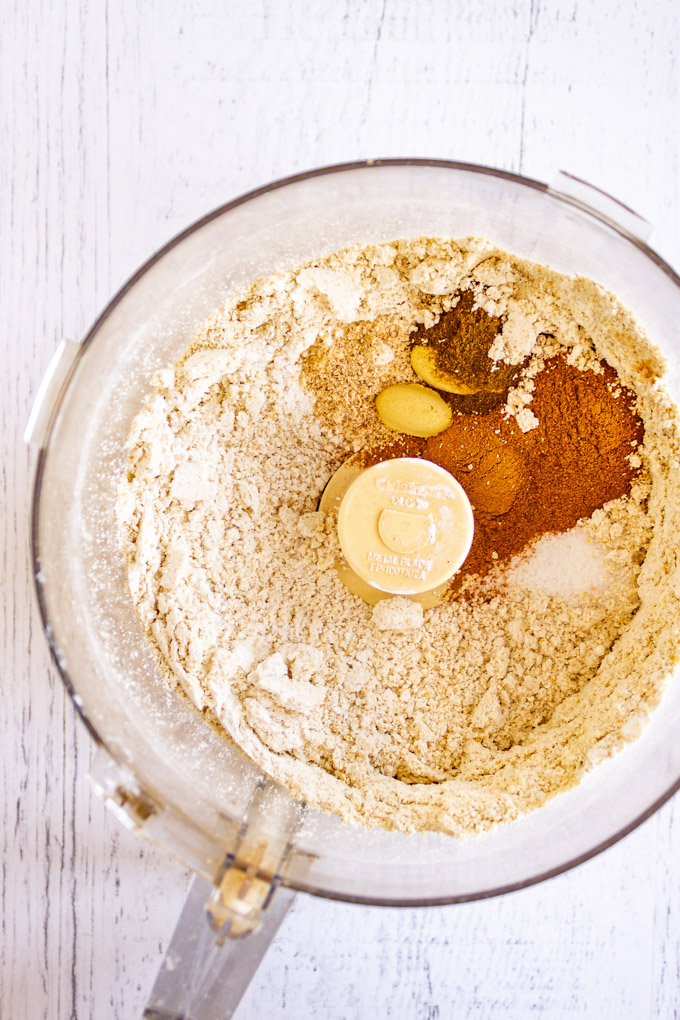 Oat flour and spices in a food processor, on a white background.