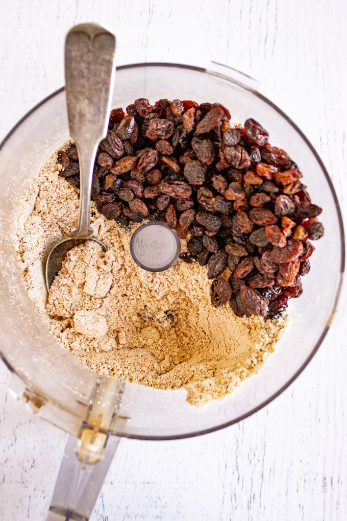 Oat flour and raisins in a food processor, on a white background.