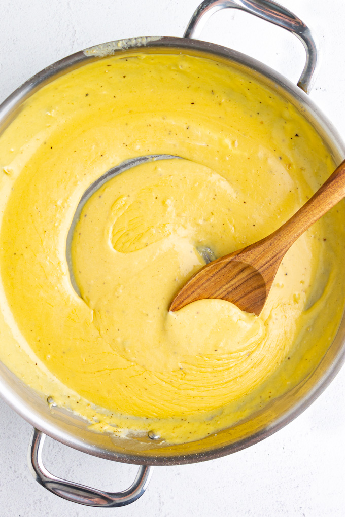 Yellow cheese sauce in a stainless steel skillet, on a white background.