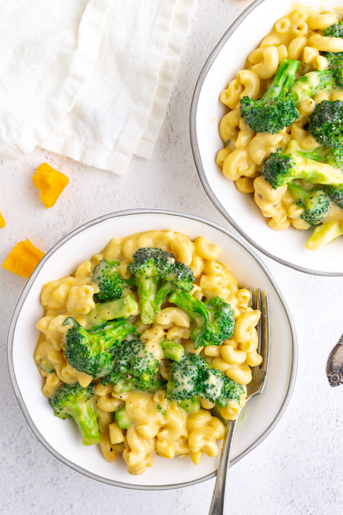 Overhead shot of creamy Healthier mac and cheese with broccoli in white bowls on a white background.