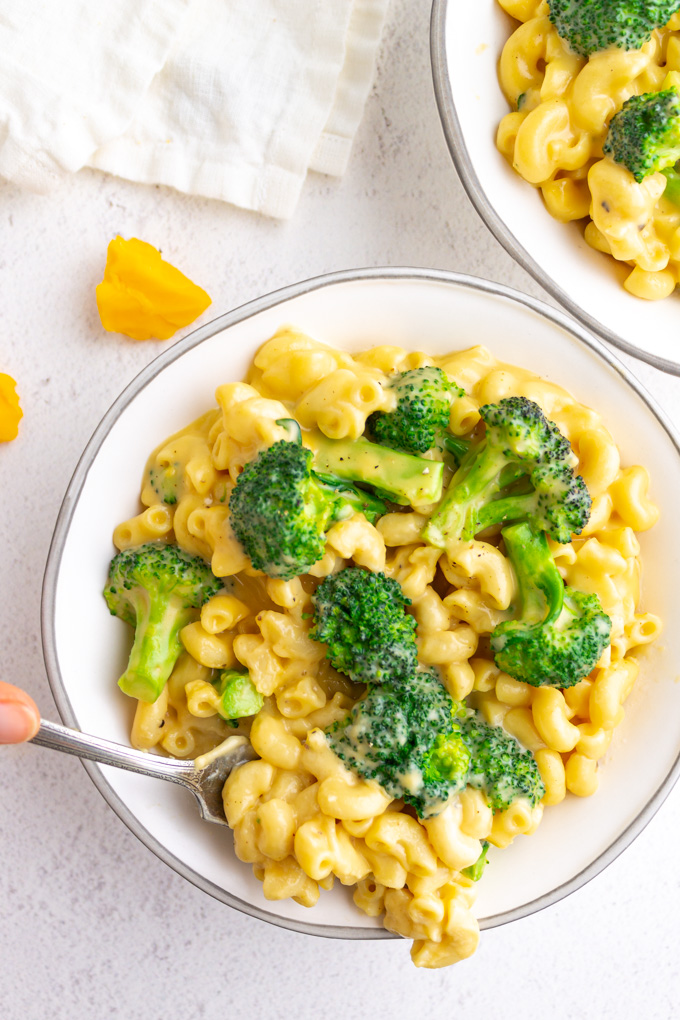 Overhead shot of healthier mac and cheese with broccoli in white bowls, with a fork serving some up.