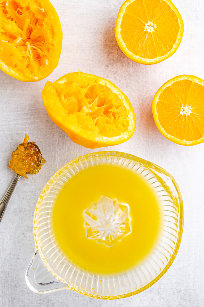 Squeezed oranges, and half un-squeezed oranges on a gray background with juice in a juicer.