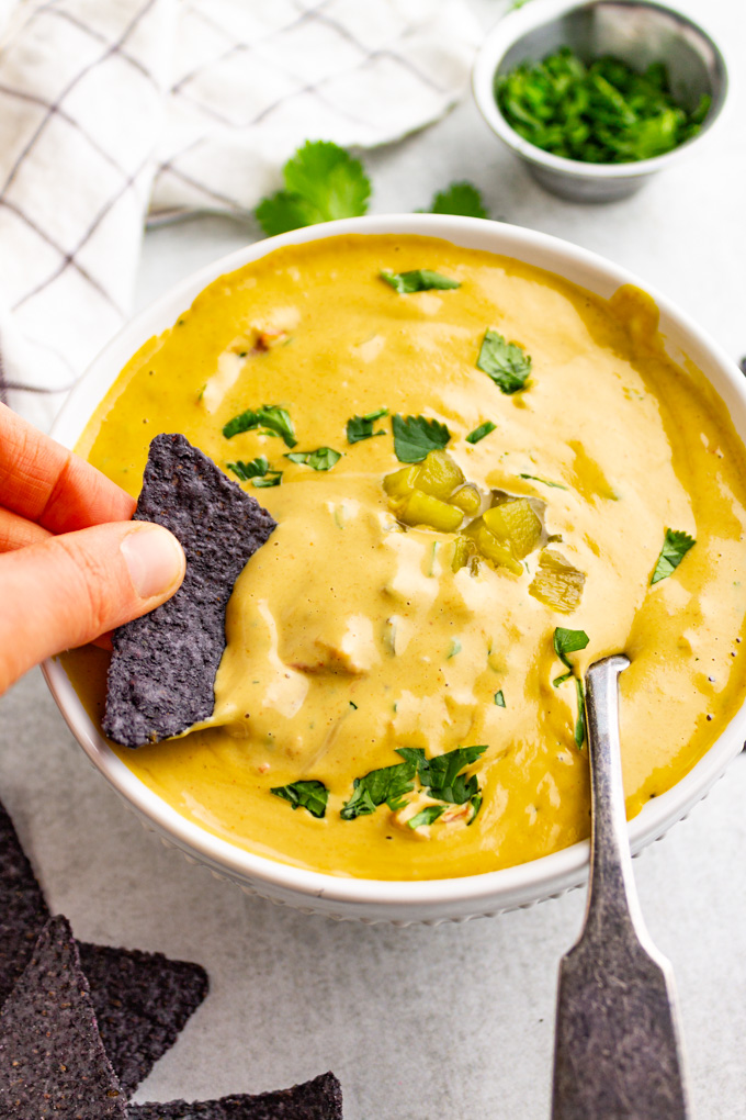 vegan cashew Queso in a white bowl with a tortilla chip dipping into it.