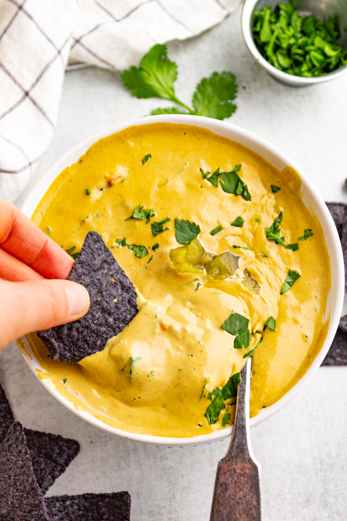 A bowl of vegan cashew queso with a tortilla chip being dipped into it.