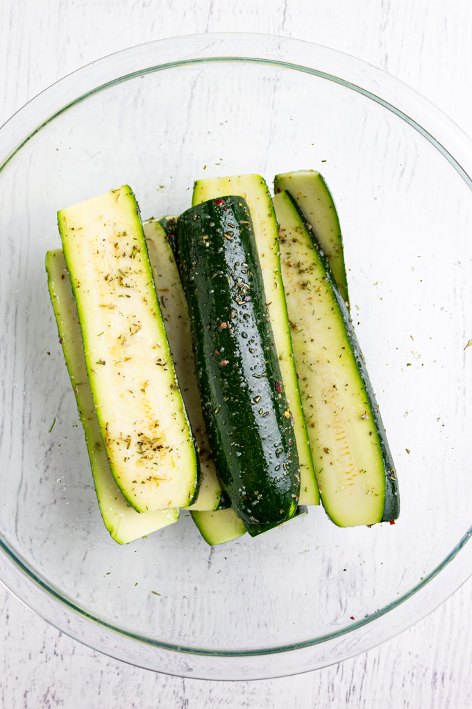 zucchini in a bowl, sliced in lengthwise, and tossed in spices and oil