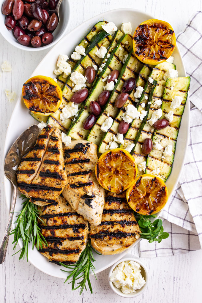 Greek grilled chicken with zucchini on a platter with olives feta cheese, and grilled lemons