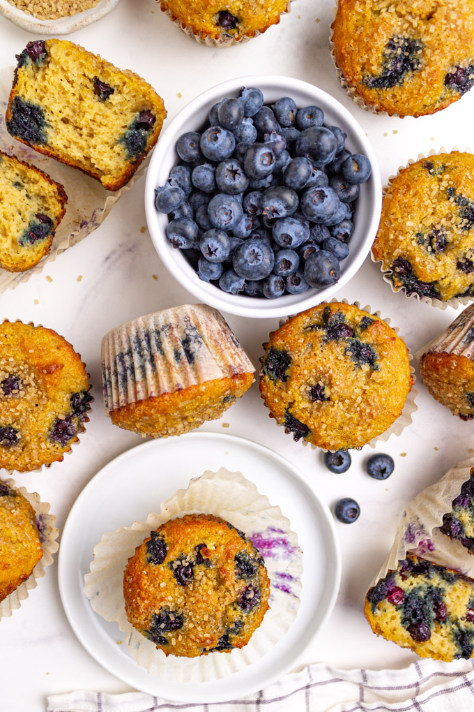 gluten free blueberry muffins scattered on a white background with a bowl of blueberries.