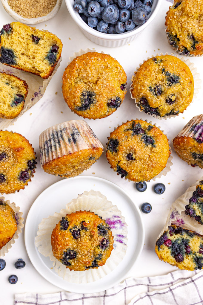Gluten free blueberry muffins on a white background, with blueberries in a bowl.