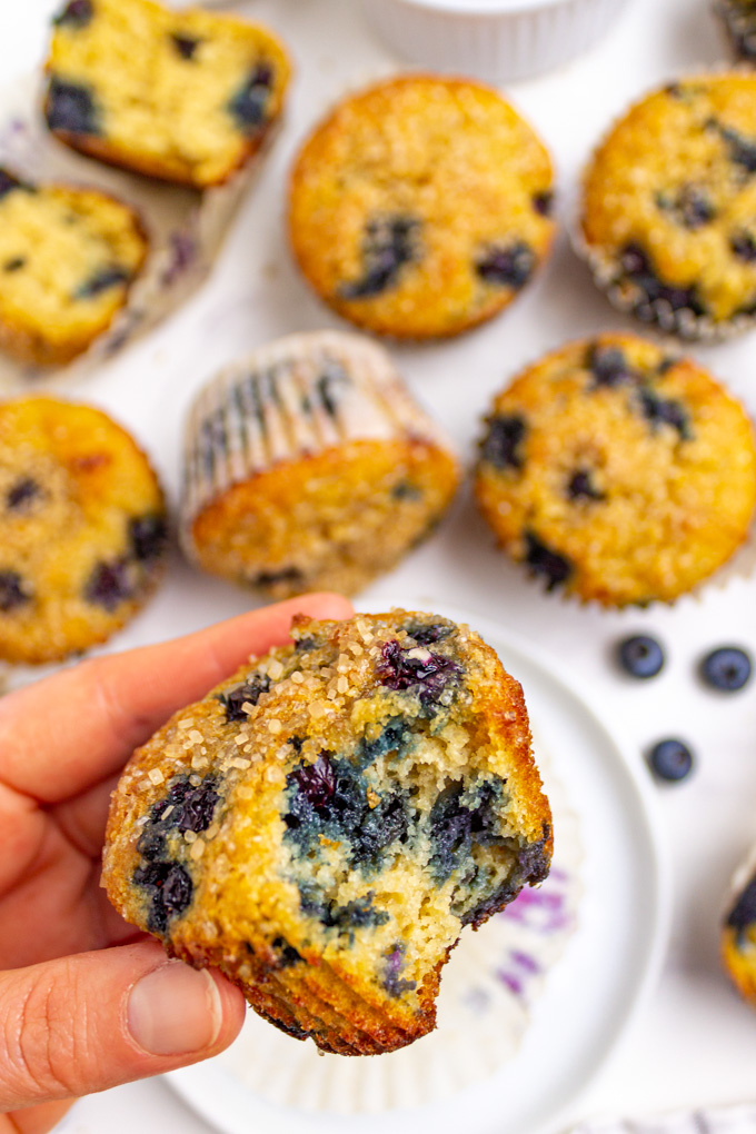 A hand holding a gluten free blueberry muffin with a bite taken out of it.