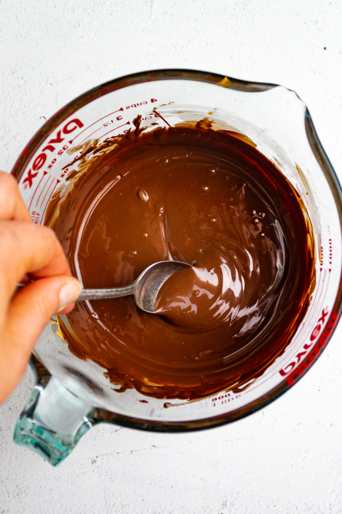 melted chocolate and butterscotch chips in a bowl with a spoon mixing it, and a hand holding the spoon.