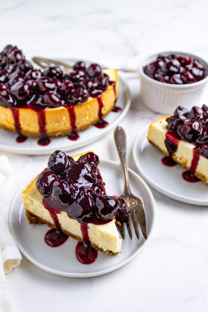 slices of instant pot cheesecake with cherry topping on white plates, on a white background.
