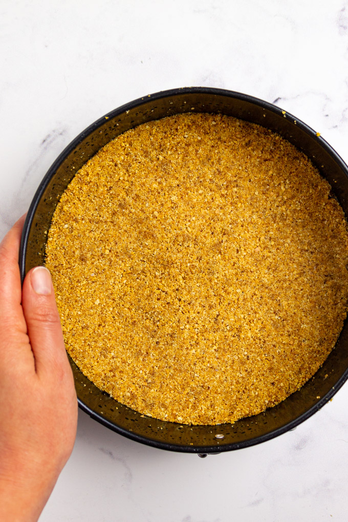 graham cracker crust in a round pan with a hand holding it.