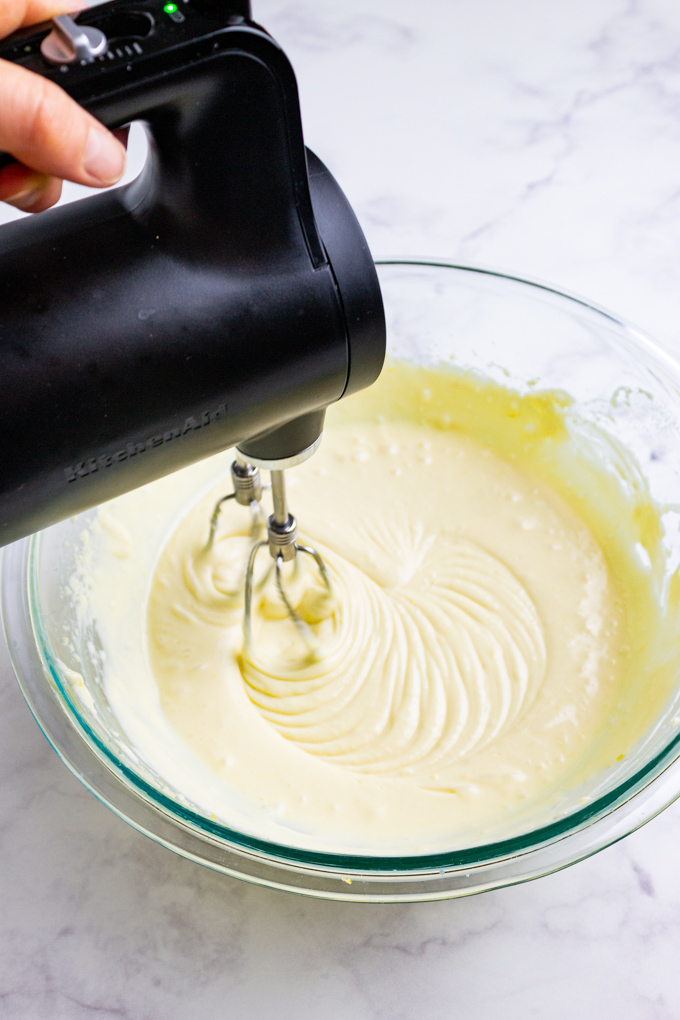 cheesecake filling in a mixing bowl being mixed by an electric hand mixer.