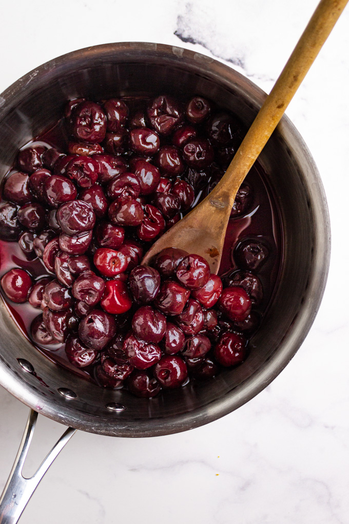 cherries in a sauce pot with a wooden spoon