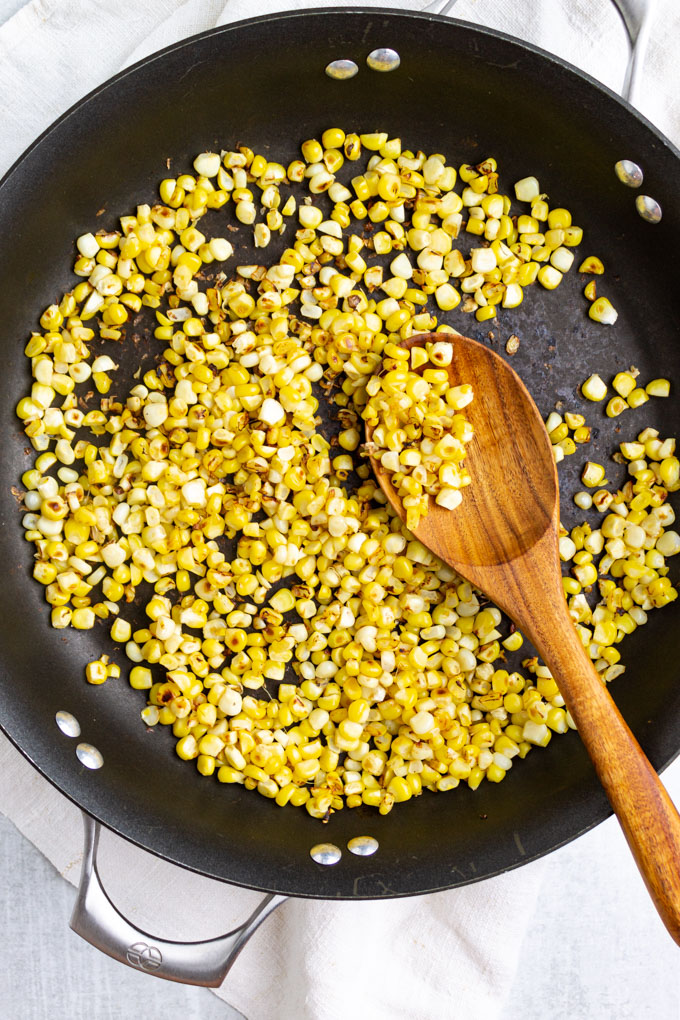 Corn cooked in a skillet with a wooden spoon