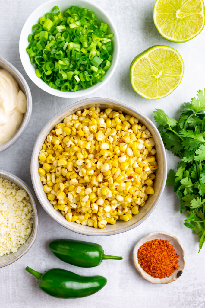 Ingredients in bowls, corn, cotija cheese, green onion, tajin, mayo, cilantro, limes, and jalapenos