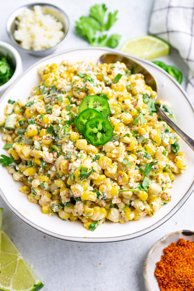 Mexican street corn salad in white serving bowl, with a few slices of jalapenos on top.