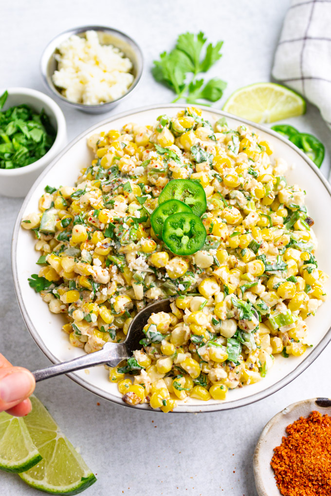 Closeup angle of Mexican street corn salad in a bowl, with a spoon scooping some out.