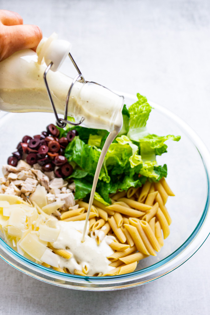 Pour shot of healthy Caesar dressing in a mixing bowl with pasta salad ingredients in it.